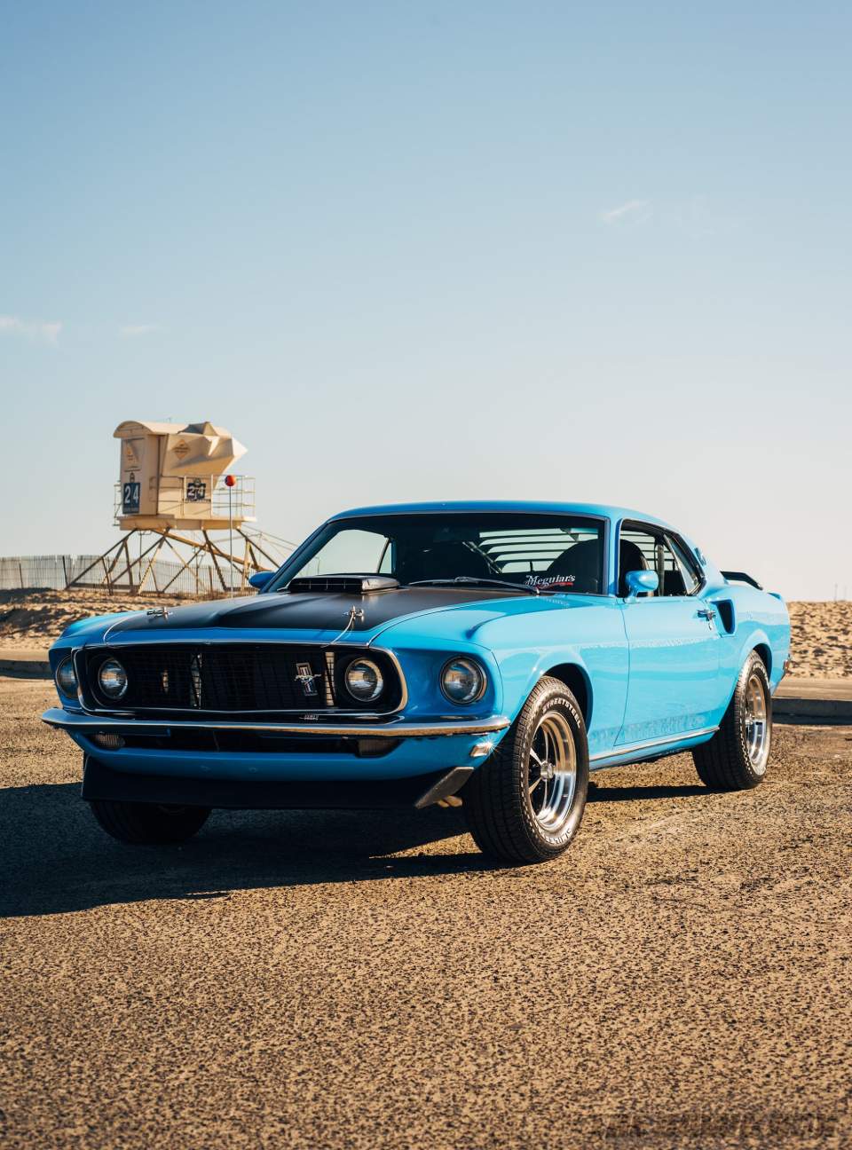 Front shot of the Blue 1969 Mustang Mach 1 parked at the beach with a lifeguard tower in the background