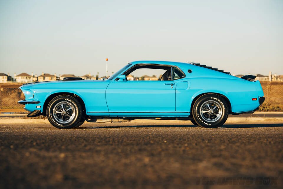 Side shot of the Blue 1969 Mustang Mach 1 at the beach with a neighborhood in the background